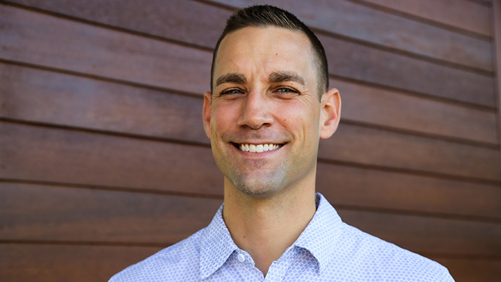 A man smiles at the camera in a collared shirt